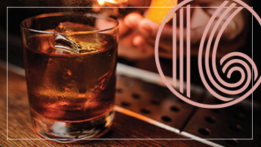 Glass of liquor on a bar next to the logo for bar 16 at The M Resort.